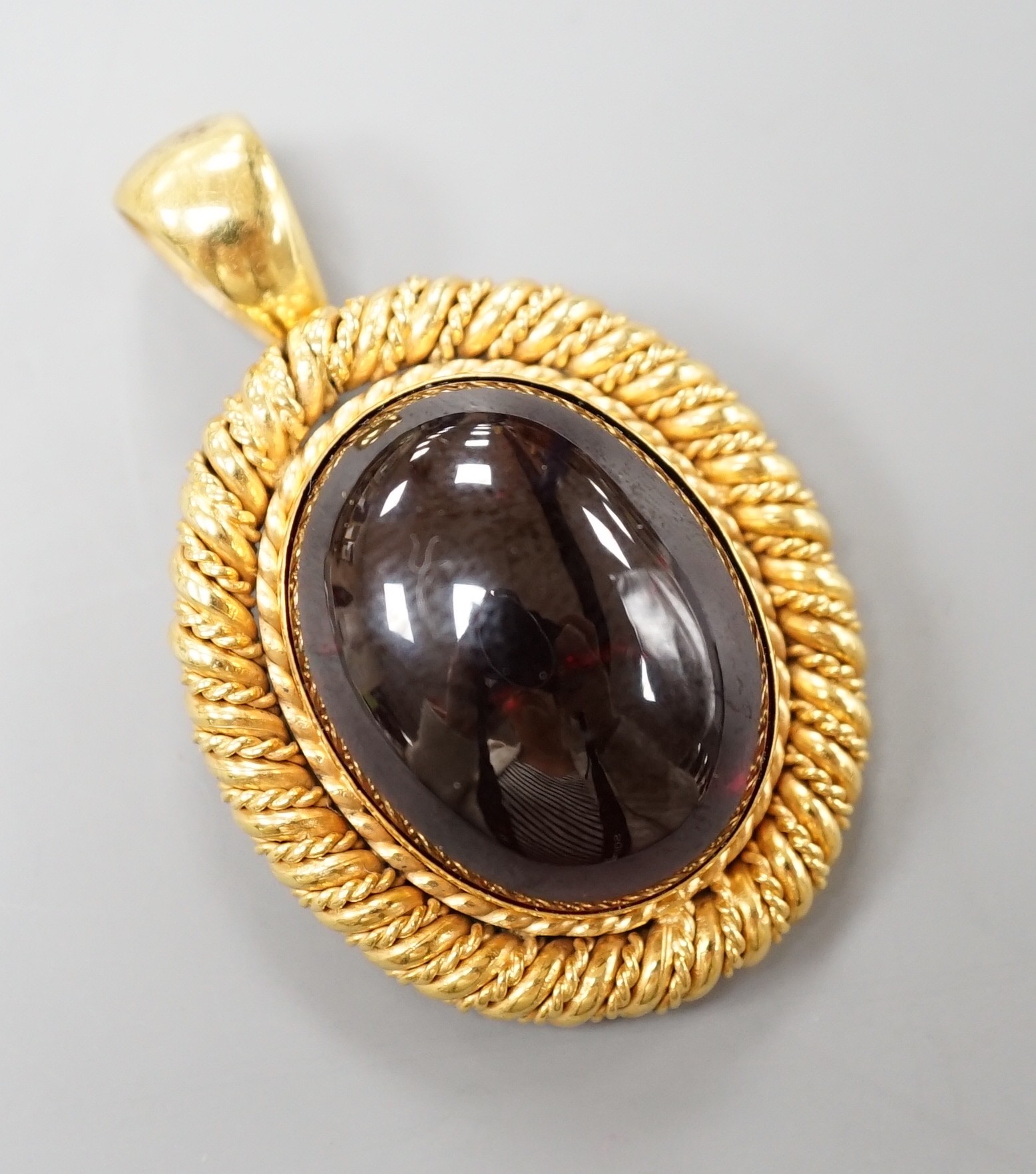 A yellow metal and oval foil backed? cabochon garnet set pendant, with close back setting, overall 42mm, gross weight 17.4 grams.